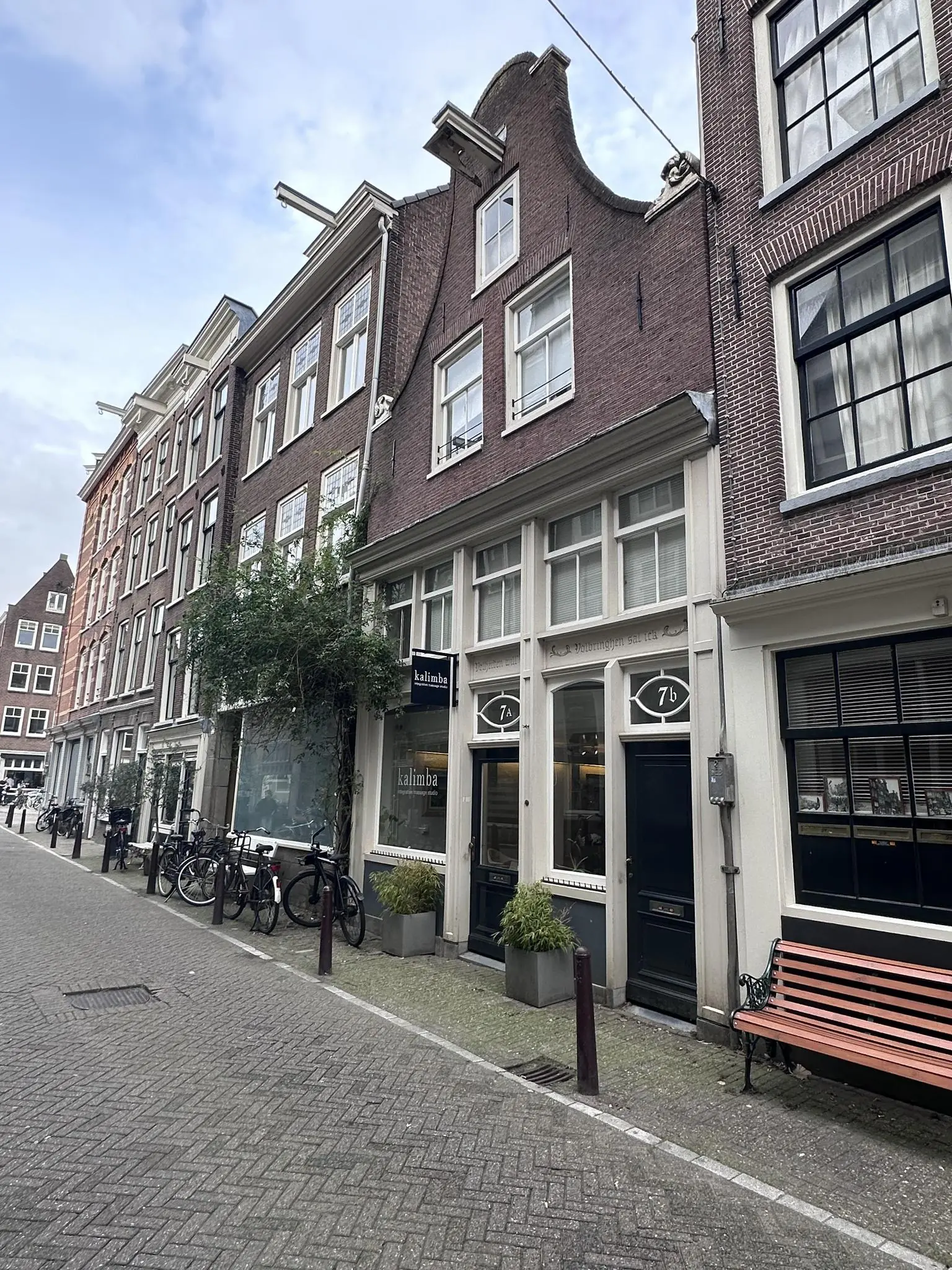 Gevels van historische panden aan de Eerste Lindendwarsstraat in Amsterdam met fietsen, een winkel en een bankje op de stoep.